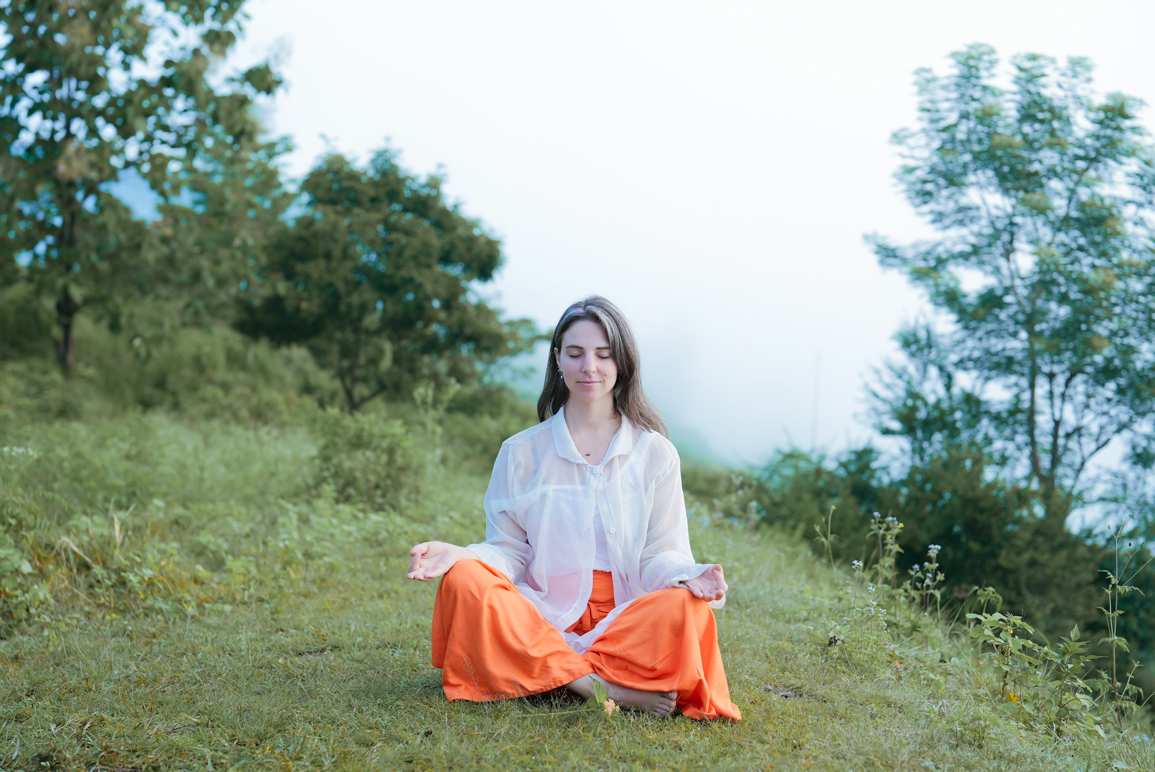 A woman meditating in a tranquil outdoor setting, surrounded by lush greenery.