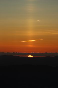 Captivating sunset over silhouetted mountains with warm hues and glowing horizon.