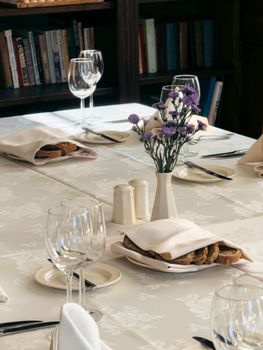 Formal dining table with wine glasses, purple flowers, and elegant tableware in a restaurant setting.