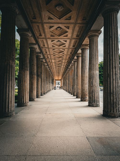 Free Symmetrical view of a historic colonnade with architectural details and people in the distance. Stock Photo