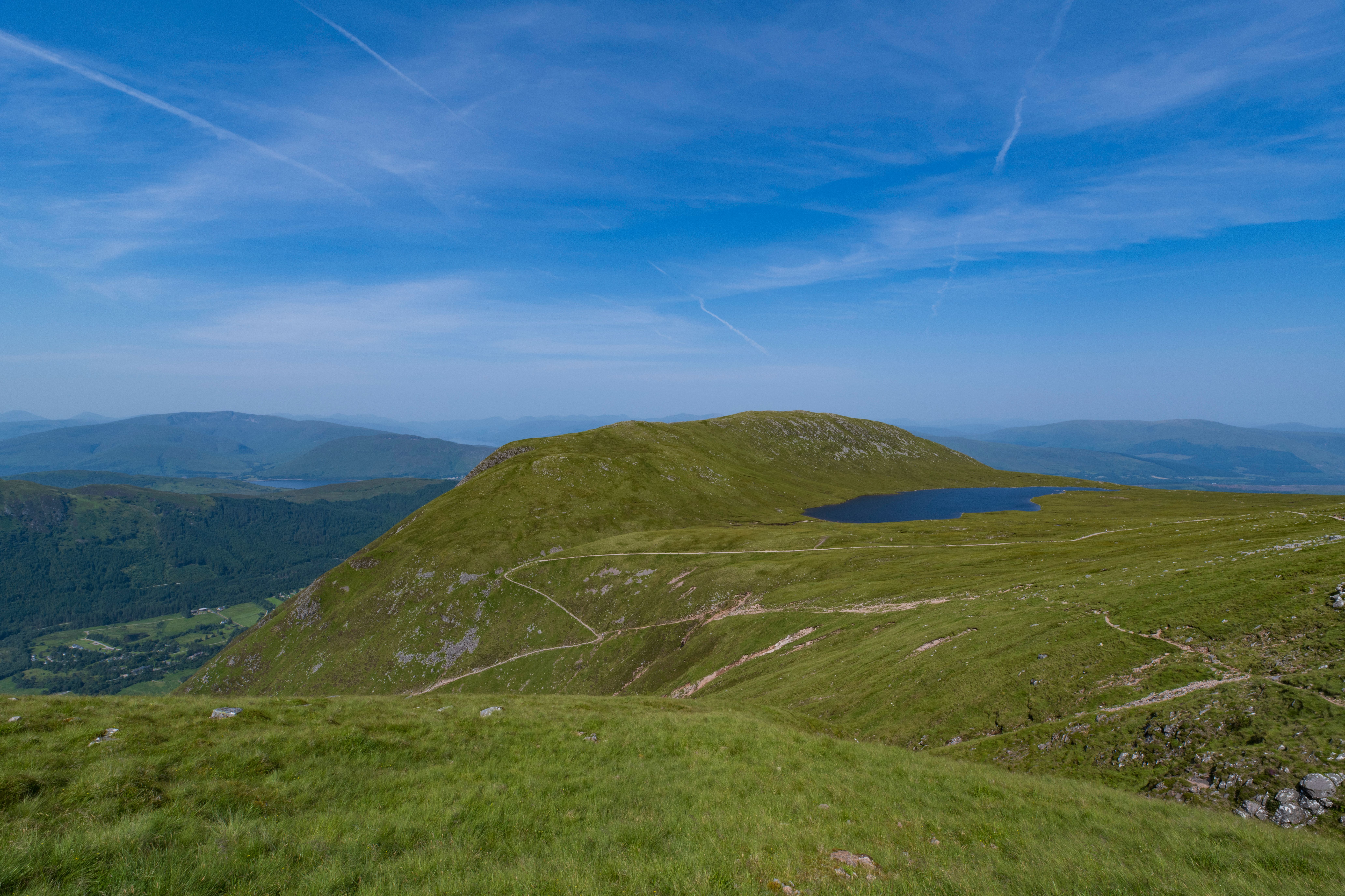 Breathtaking view of the Scottish Highlands with rolling hills, a serene loch, and expansive blue skies.