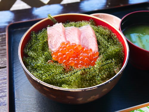 High angle of bowl with sashimi with red caviar and tobiko placed on wooden tray