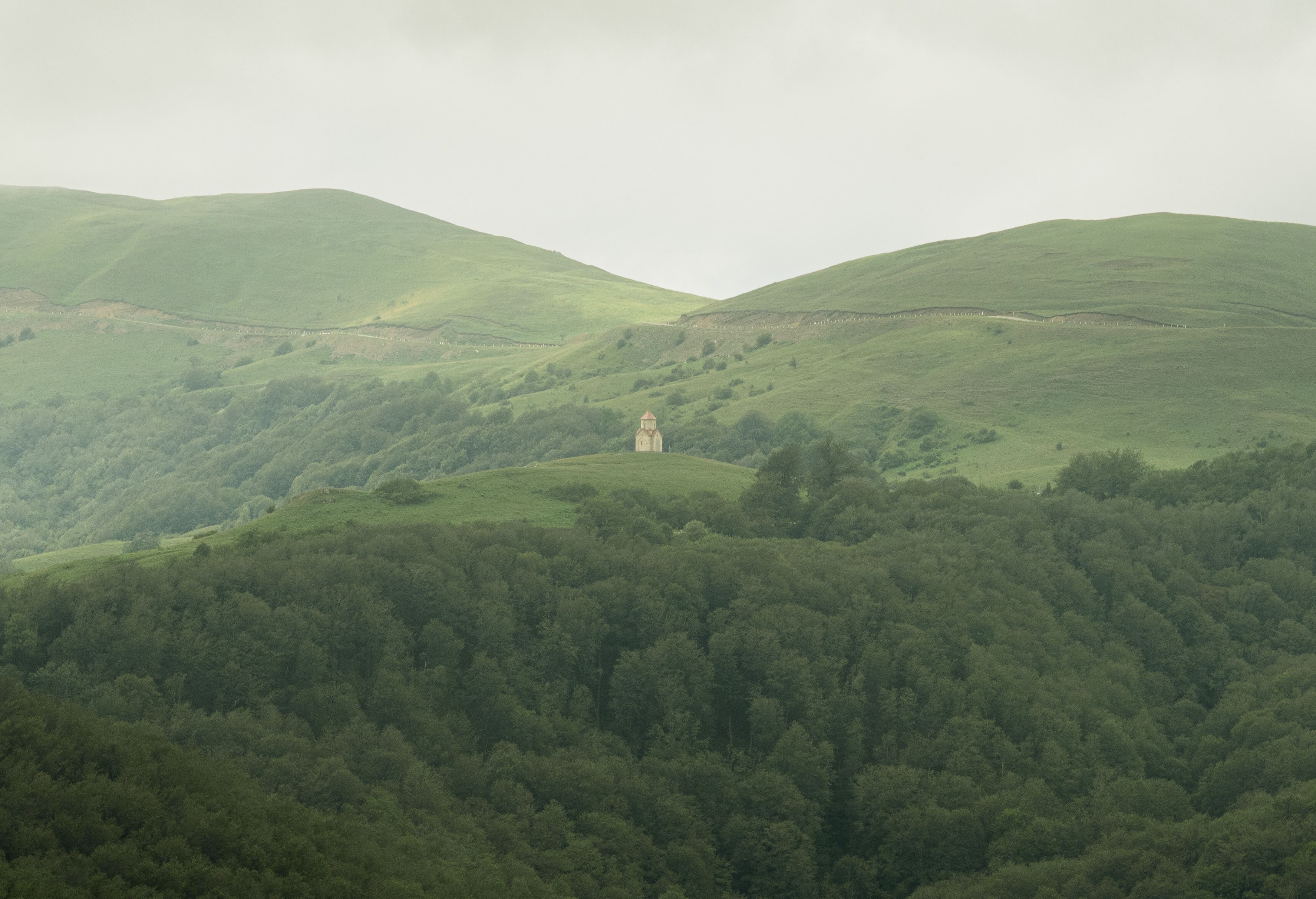 A serene landscape of lush Georgian hills with a solitary chapel amidst the greenery, evoking tranquility.
