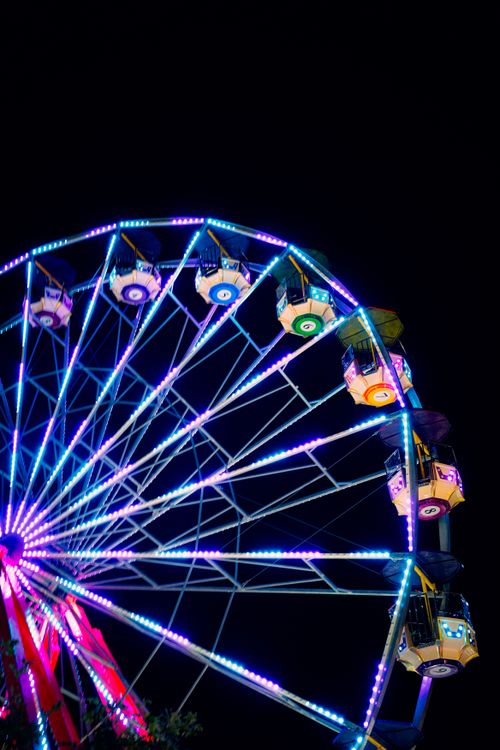 Free A colorful Ferris wheel lit up with neon lights against a dark night sky, capturing the vibrant mood of a carnival. Stock Photo