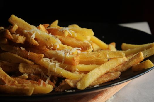 Golden French fries topped with grated cheese on a dark plate, perfect for snack time.