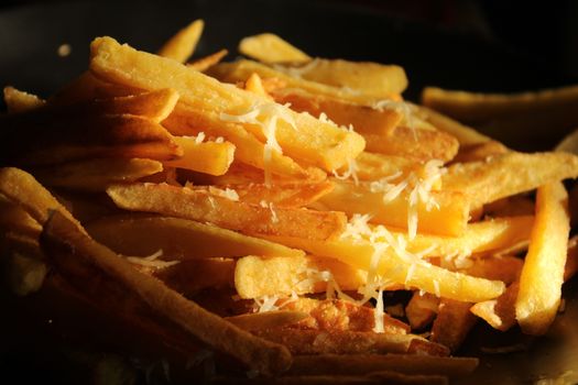 Golden crispy French fries topped with freshly grated cheese in warm lighting.