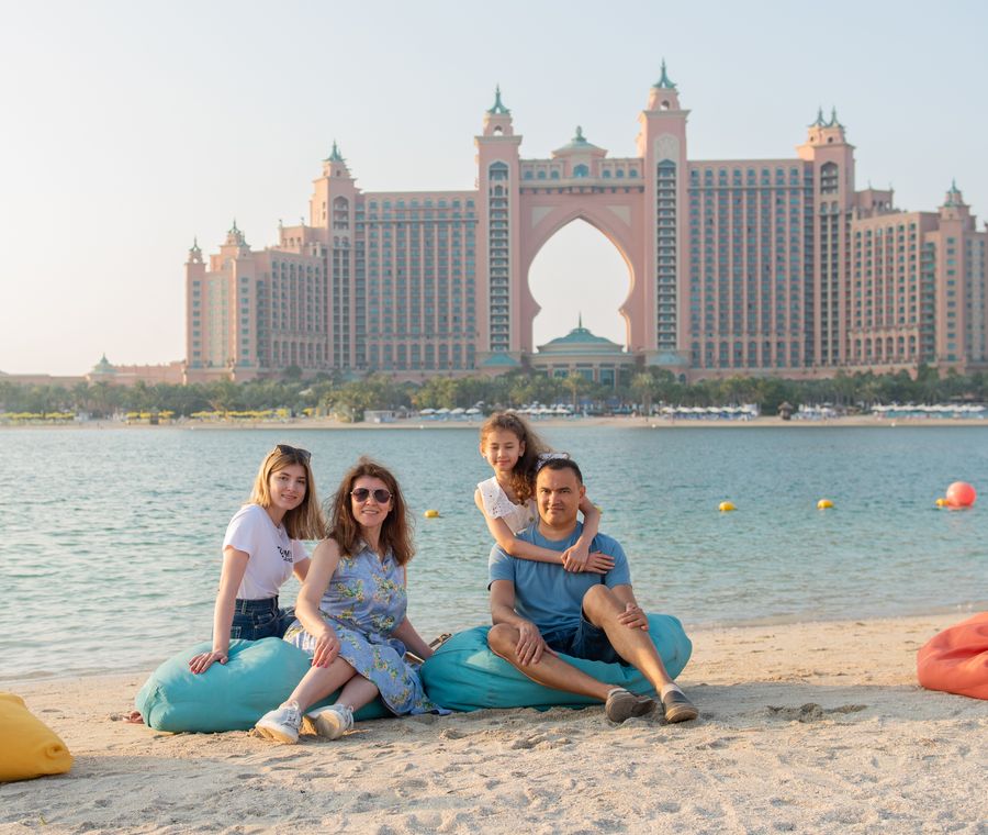 Family relaxing on a sandy beach with the iconic Atlantis, The Palm hotel in Dubai, UAE in the background.