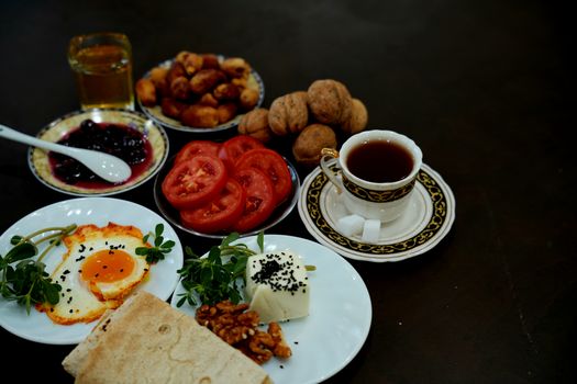 A rich Iranian breakfast spread featuring tea, bread, eggs, fresh tomatoes, jam, and walnuts.