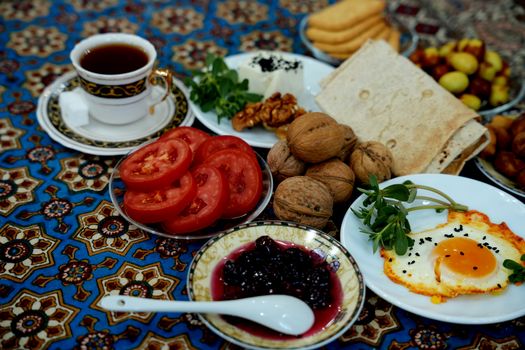 A vibrant Persian breakfast spread featuring tea, bread, nuts, eggs, and vegetables on a colorful cloth.