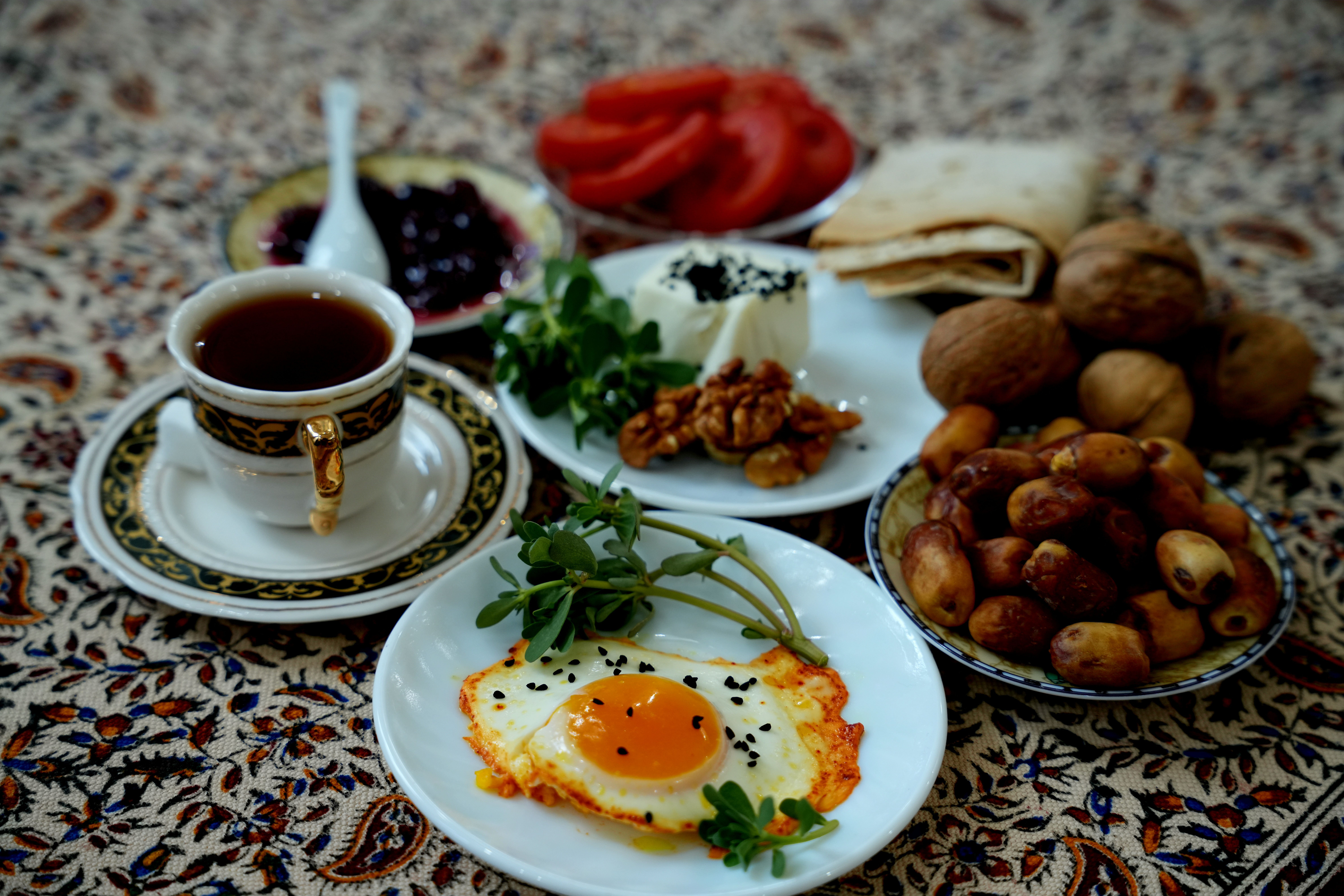 A vibrant Persian breakfast spread featuring tea, fried eggs, dates, and walnuts on patterned fabric.