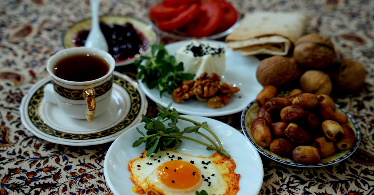 A vibrant Persian breakfast spread featuring tea, fried eggs, dates, and walnuts on patterned fabric.