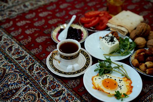 A traditional Persian breakfast with eggs, tea, tomatoes, cheese, and walnuts on a decorative tablecloth.