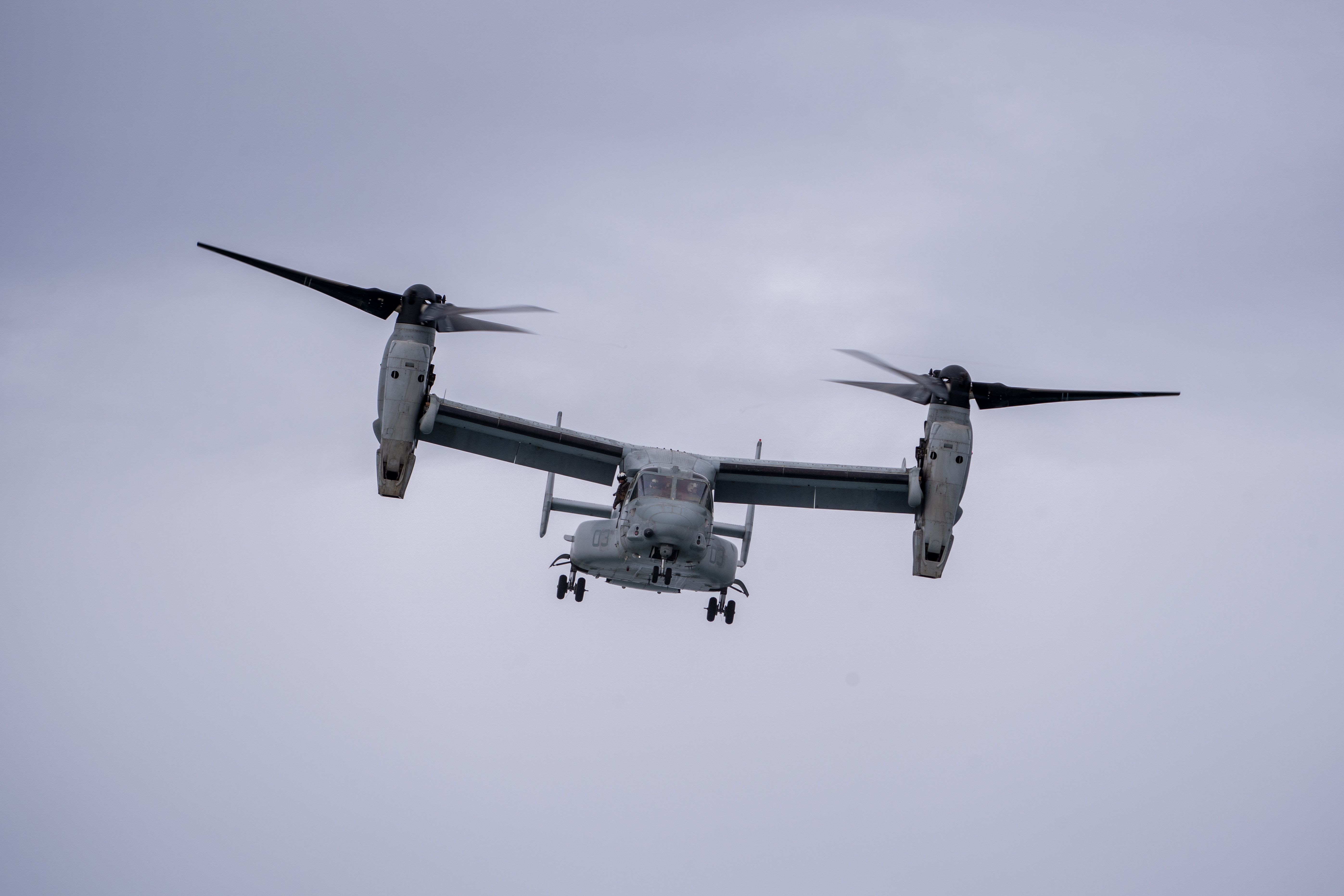 V-22 Osprey tiltrotor aircraft flying through cloudy sky, wings horizontally configured.