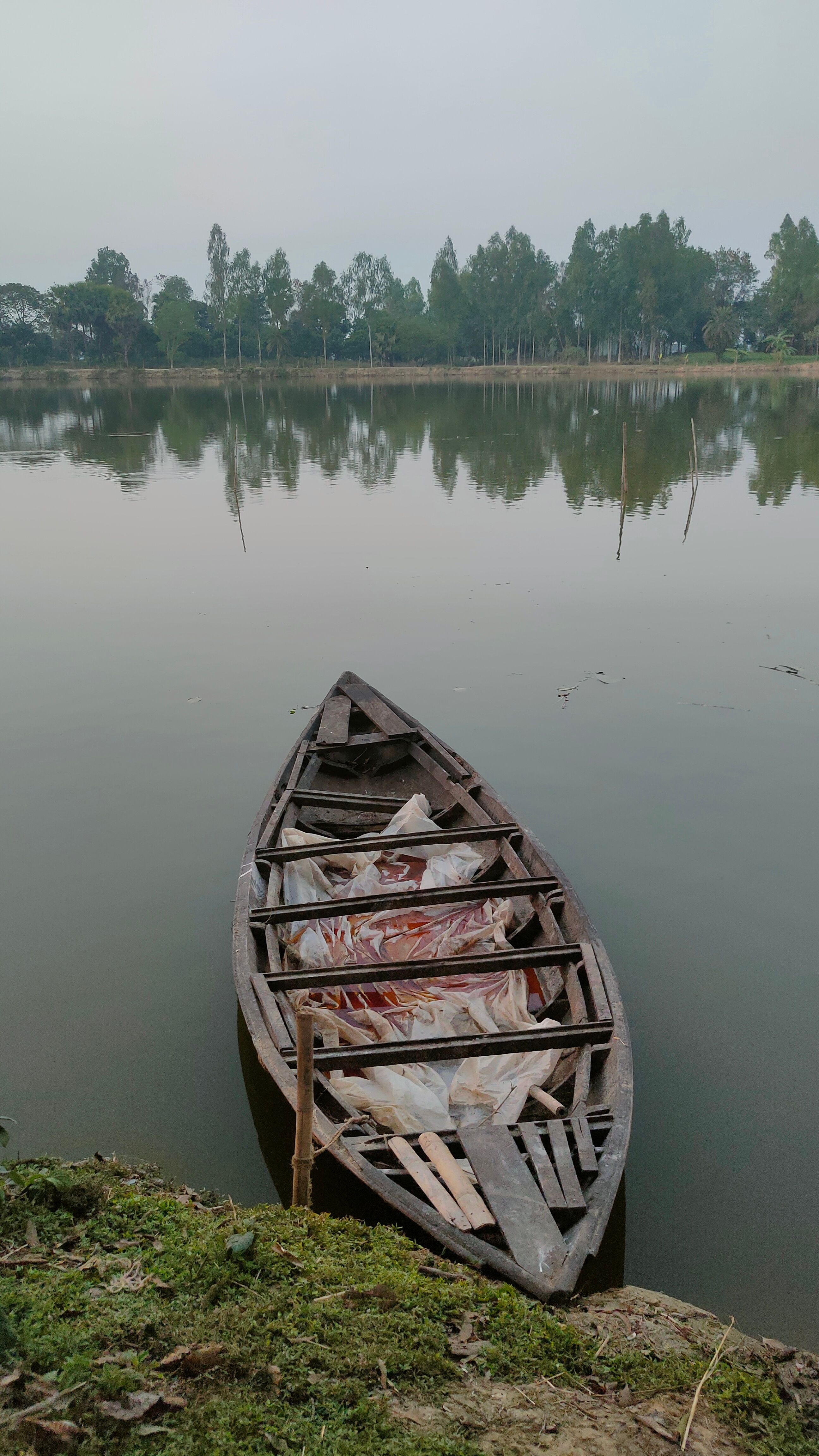 A wooden boat rests peacefully on a calm lake surrounded by lush greenery, creating a serene and reflective scene.