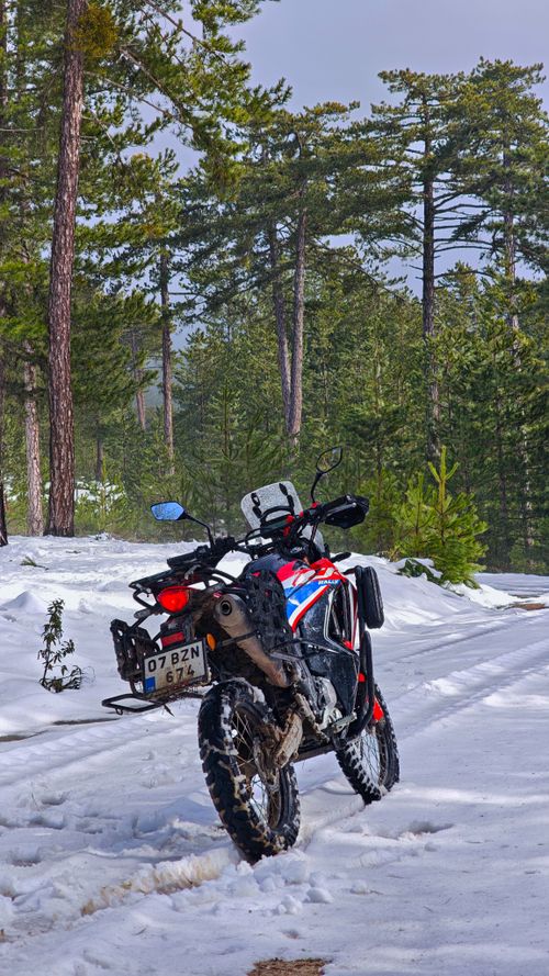 Free A motorcycle parked in a snowy forest, ready for an adventure trip under a winter sky. Stock Photo