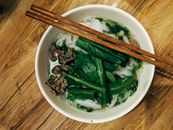 Top view of a bowl of Vietnamese pho with fresh herbs and chopsticks on a wooden table.