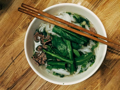 Top view of a bowl of Vietnamese pho with fresh herbs and chopsticks on a wooden table.