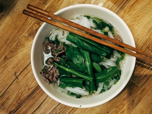 Free Top view of a bowl of Vietnamese pho with fresh herbs and chopsticks on a wooden table. Stock Photo