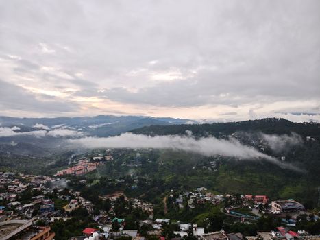 Scenic aerial view of a foggy mountain town at dawn with lush green hills and scattered clouds.