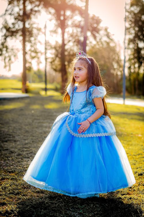 Free A young girl in a blue princess dress enjoying a sunny day outdoors. Stock Photo