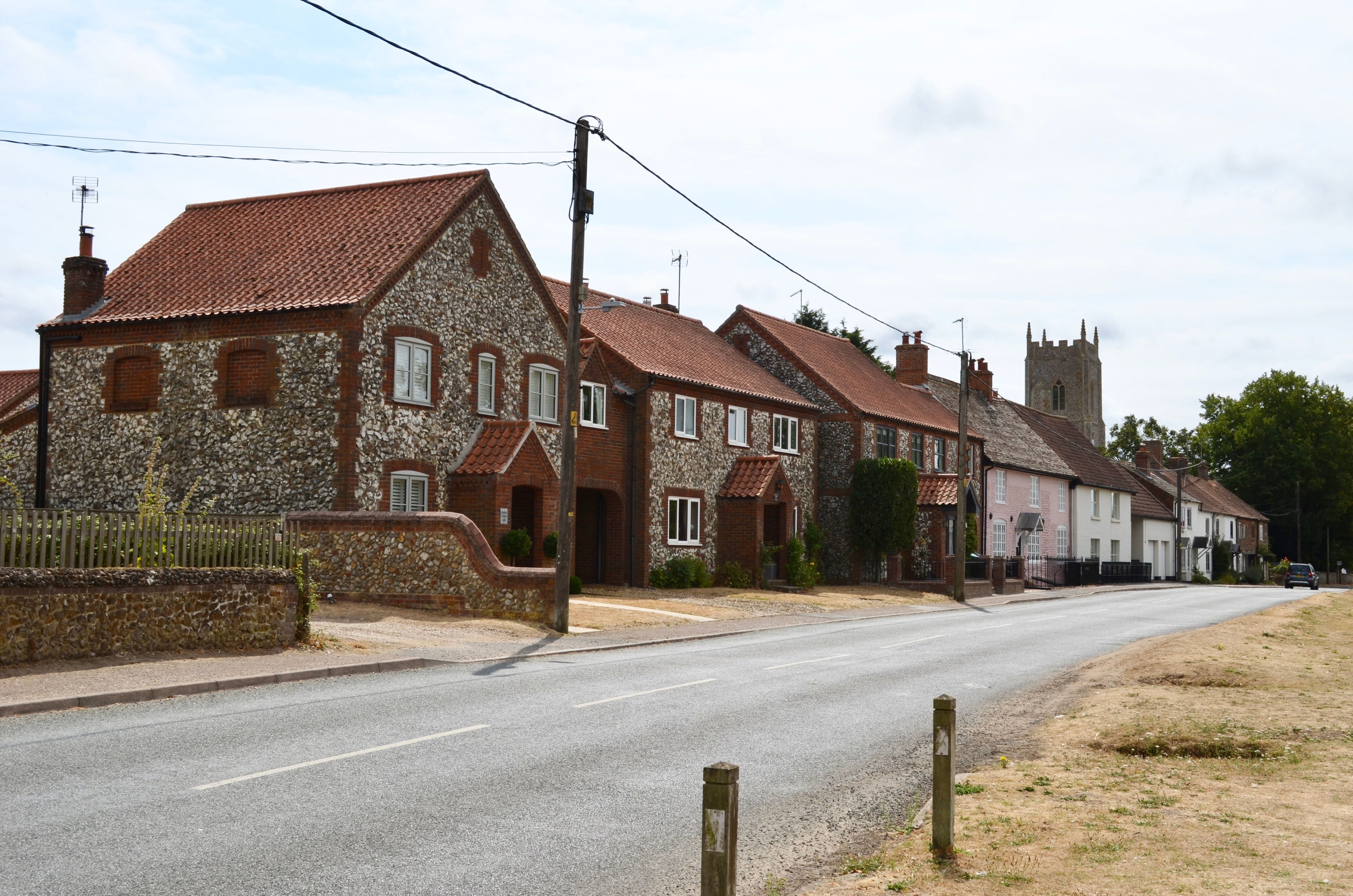 Charming street in an English village featuring traditional brick and flint houses with a church tower in the background.