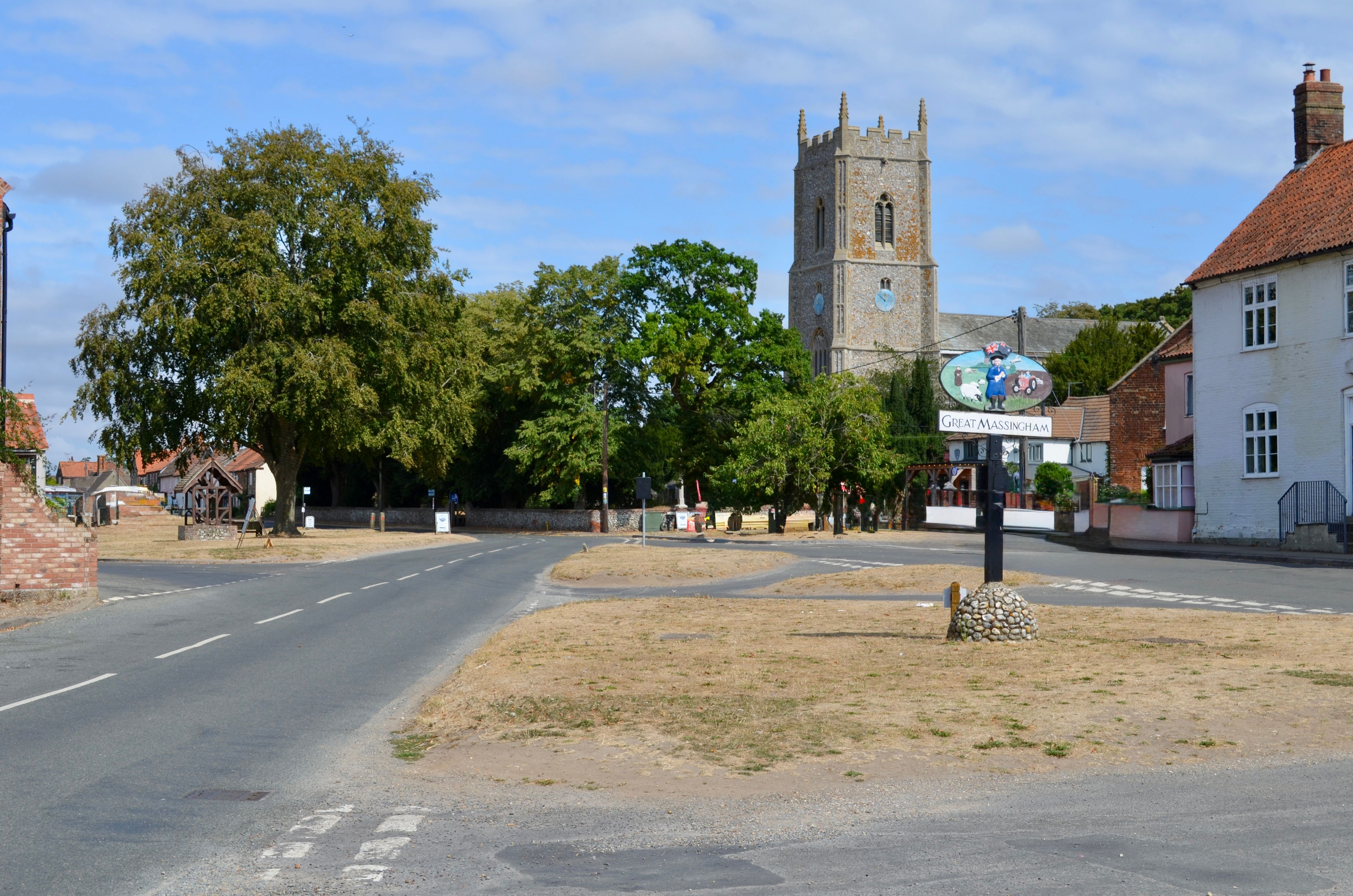 Scenic view of Great Massingham village road with historic church tower and lush trees.