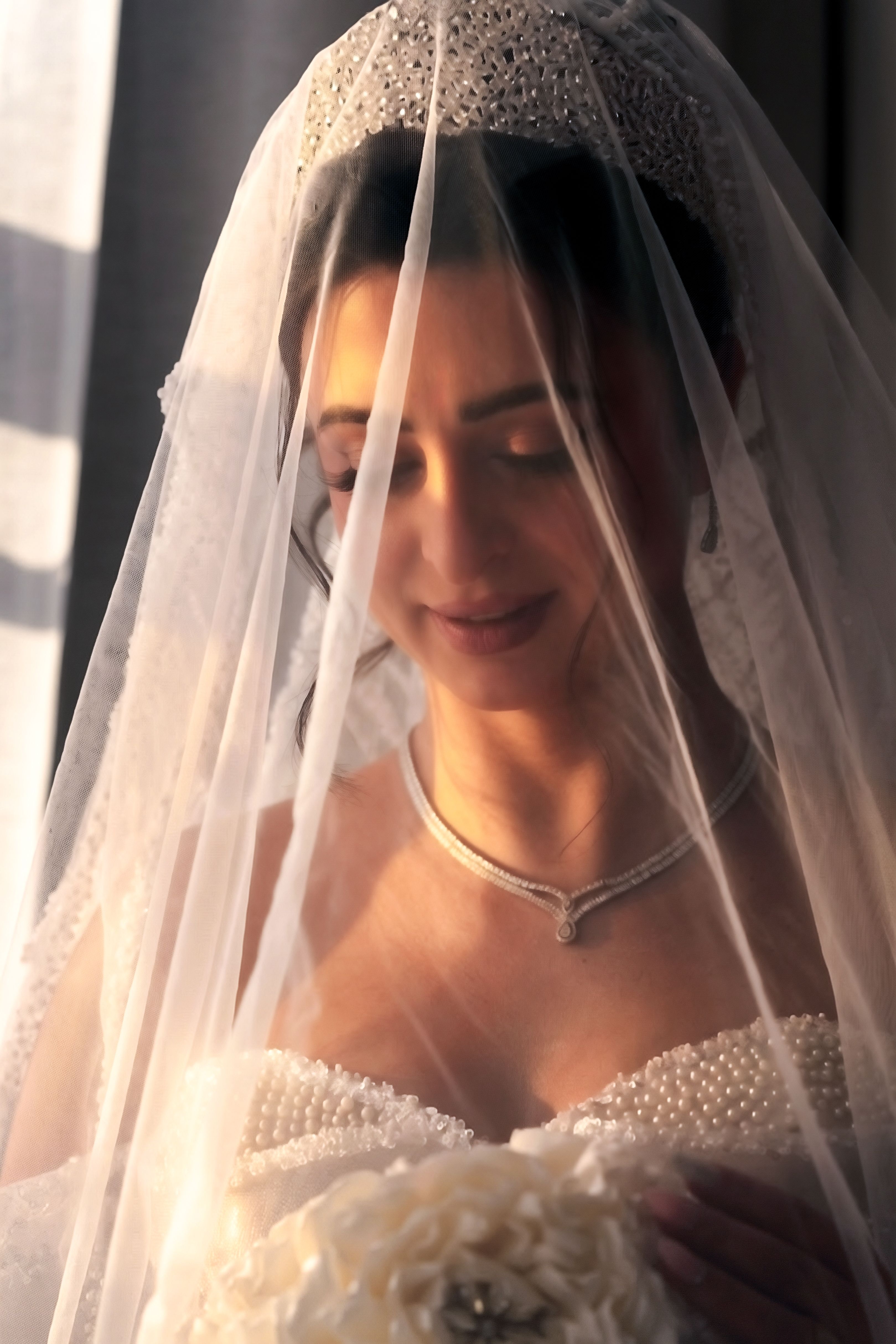 A serene bride under a lace veil, basking in warm sunlight on her wedding day.