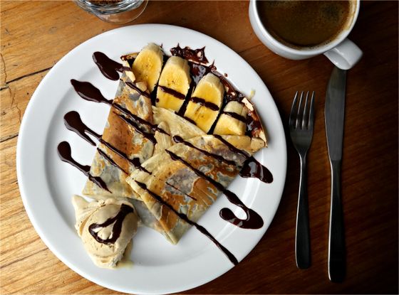 Folded crepe topped with banana slices, zigzag chocolate sauce and a scoop of coffee ice cream