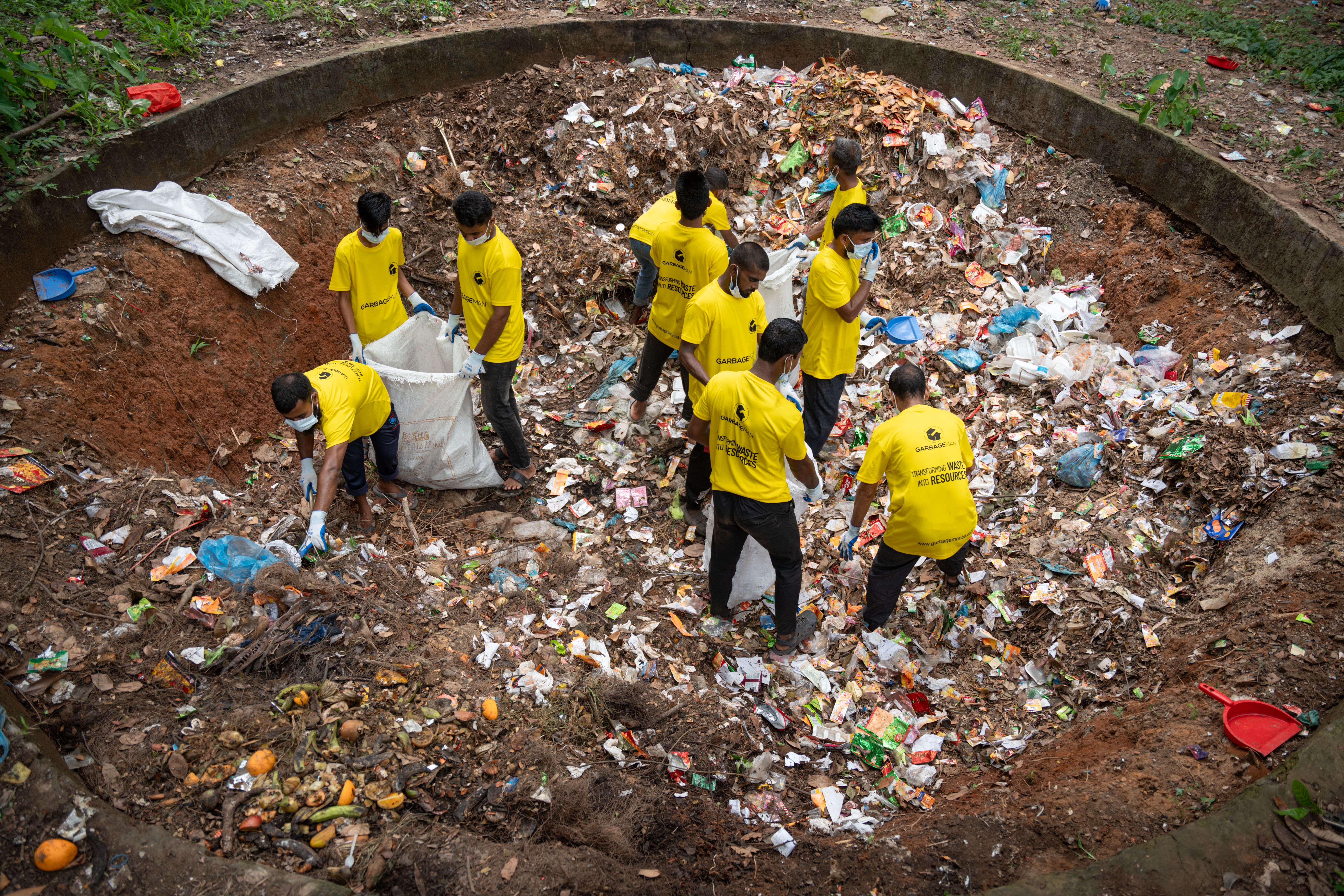 A group of volunteers in yellow shirts clean up a large waste pit outdoors, demonstrating teamwork and environmental care.