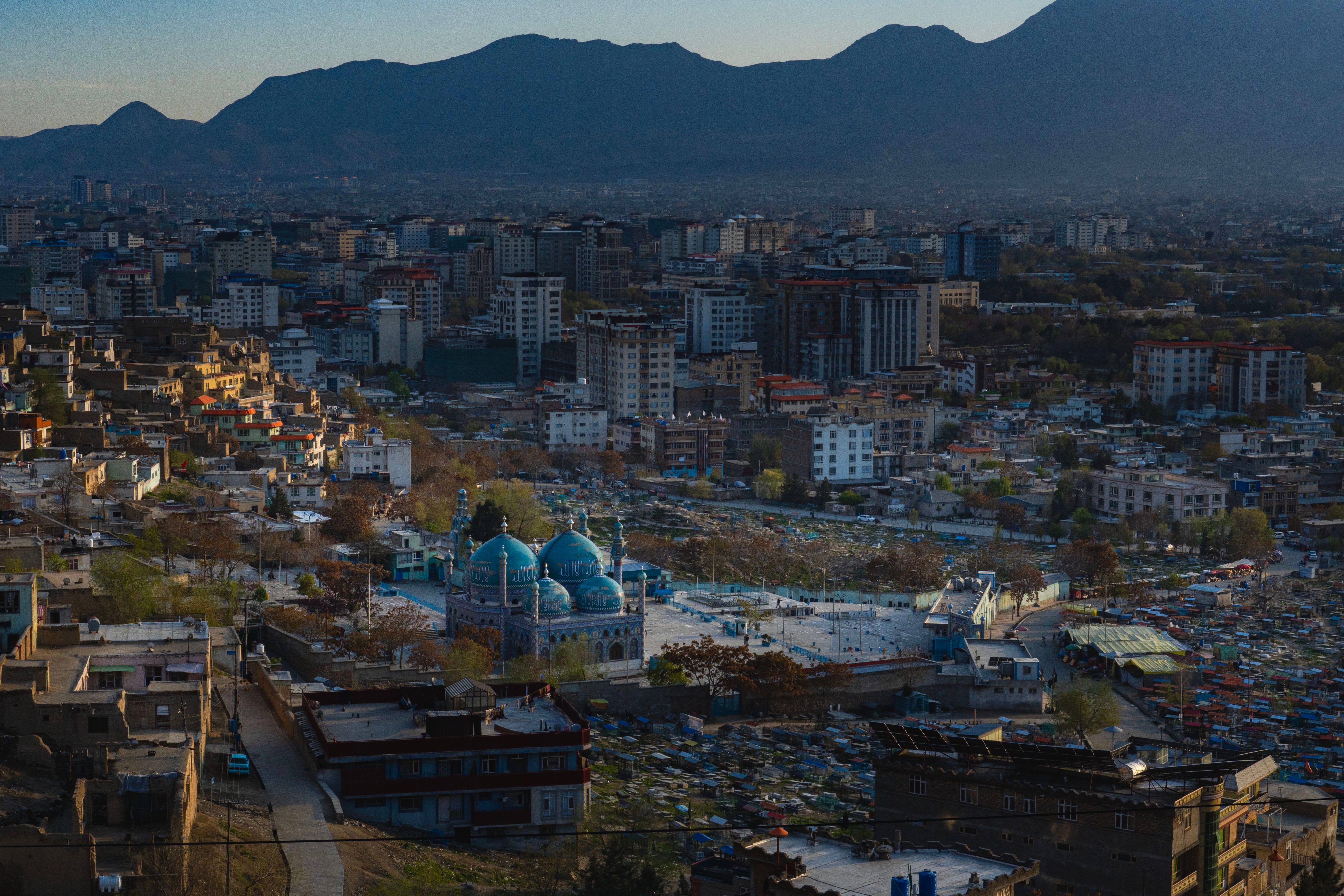 Skyline view of Kabul featuring a prominent blue mosque with the cityscape and mountains in the background.