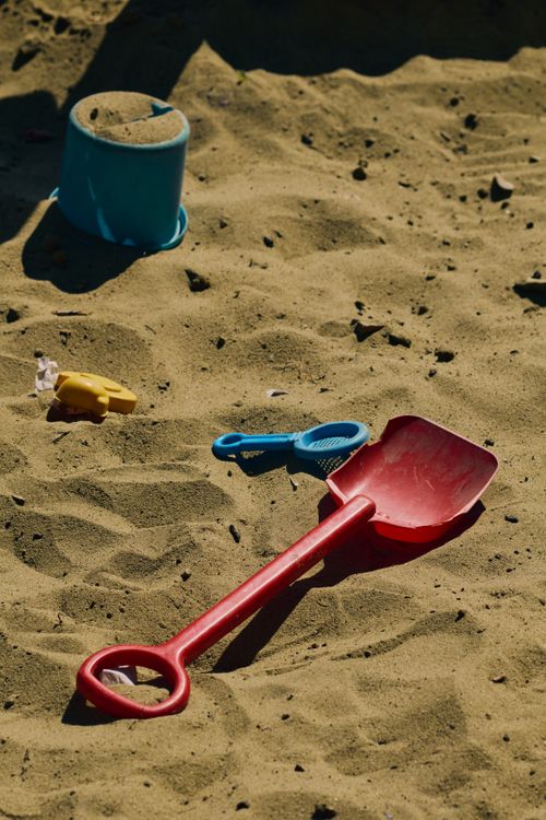 Free Colorful sand toys including a shovel on sunny beach sand, ideal for family vacation themes. Stock Photo