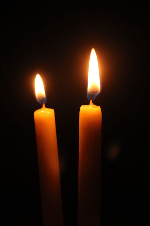 Free Two lit candles casting a warm glow in dark surroundings. Stock Photo