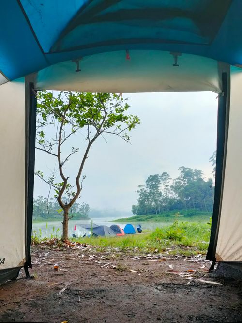 Free View from a tent overlooking a serene lakeside campsite with lush surroundings. Stock Photo