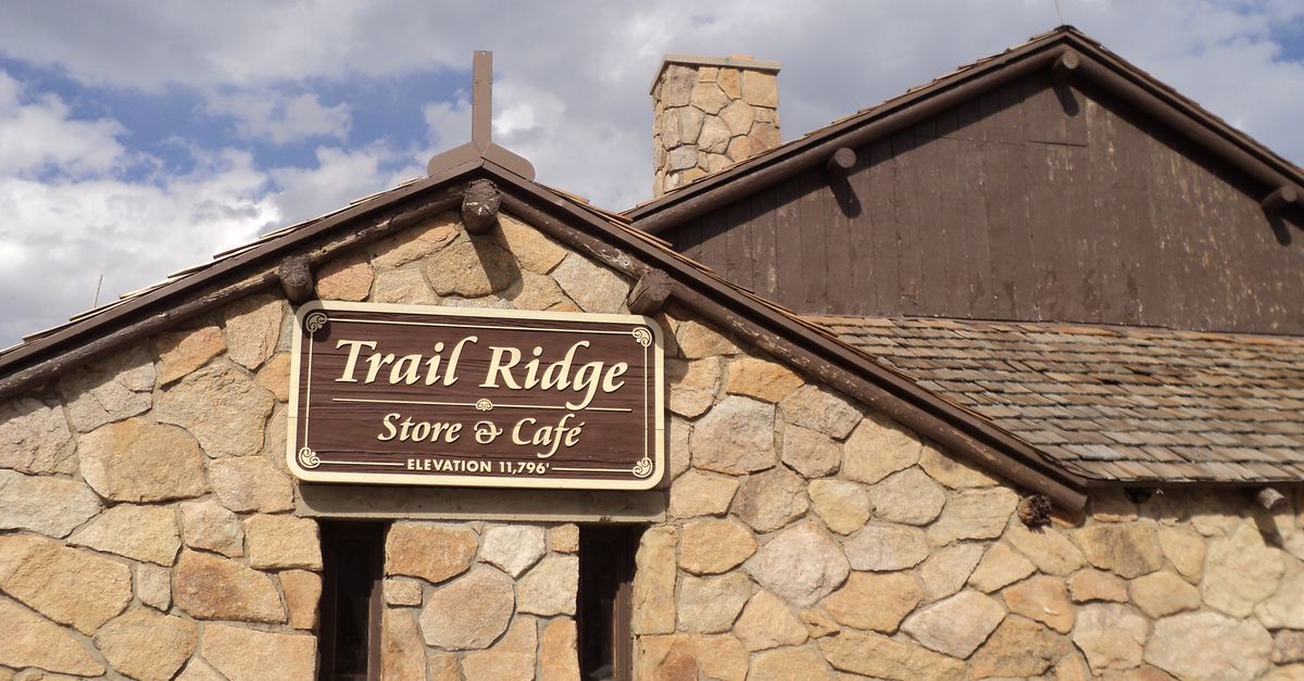 Rustic stone exterior of Trail Ridge Store & Café with elevation sign, set against a cloudy sky.