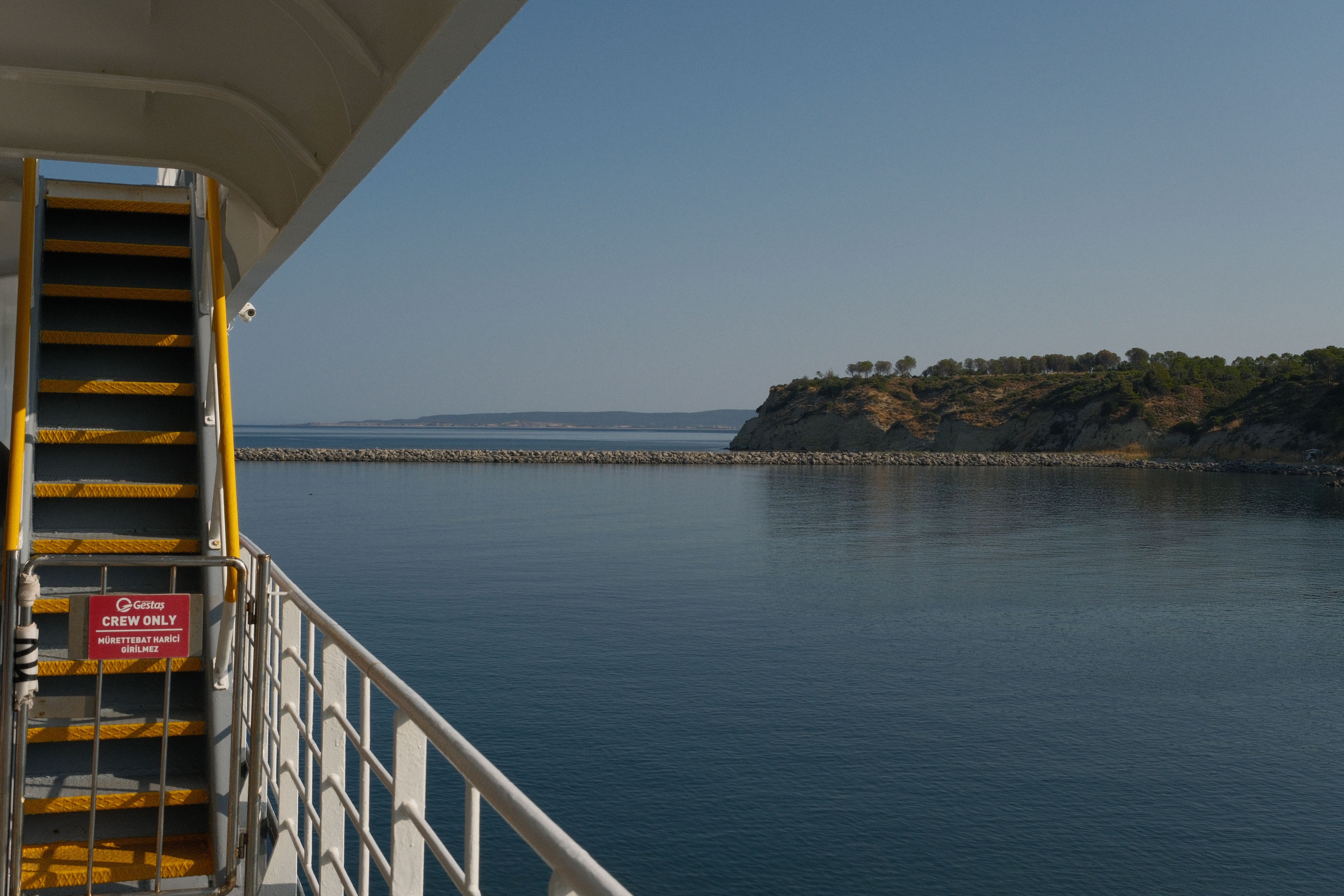 Quiet sea view from a ferry boat with a distant hilly shoreline under a clear sky.