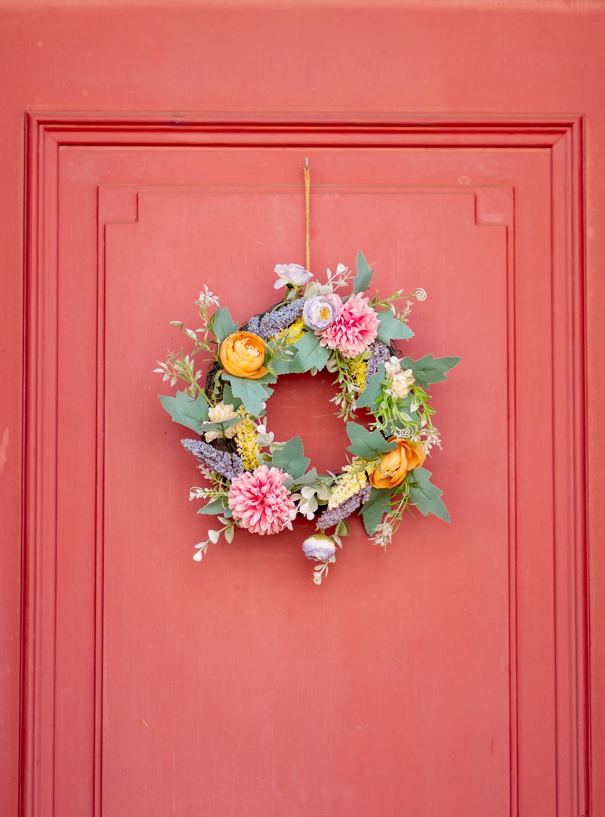 Colorful wreath with assorted flowers on a red door, creating a vibrant spring display in Lübeck, Germany. Stock Photo.
