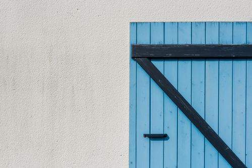 Free Simple blue wooden door with diagonal black hinge on a textured white wall. Stock Photo
