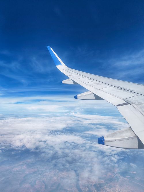 Free View of airplane wing with scenic cloudscape and blue sky, captured from window. Stock Photo