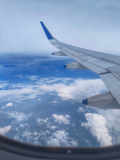 Free View from airplane window showing wing and clouds, captured during daytime flight. Stock Photo