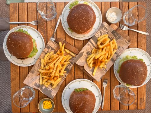 Free Delicious burgers and crispy fries served on a wooden table setting outdoors, perfect for a casual meal. Stock Photo