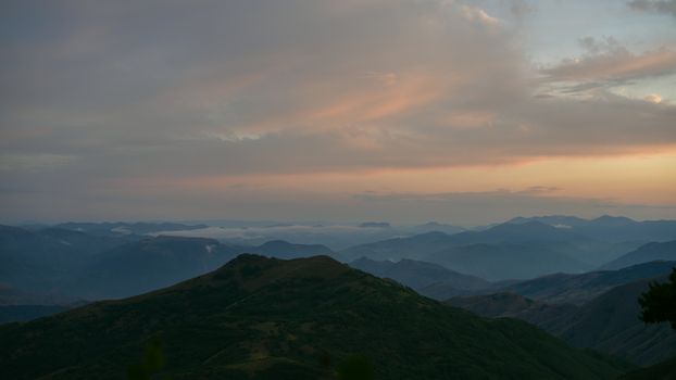 Capturing the peaceful serenity of mountain ranges during sunrise with soft pastel skies.