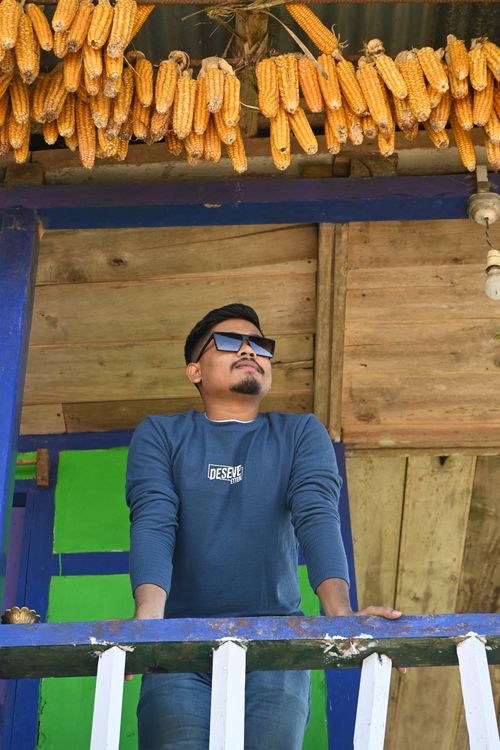 Free A man wearing sunglasses enjoying a sunny day on a rustic balcony lined with hanging corn. Stock Photo