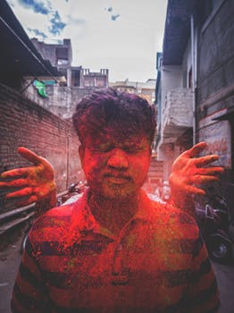 Ethnic man with closed eyes with palms behind throwing bright red paint during traditional Holi Festival