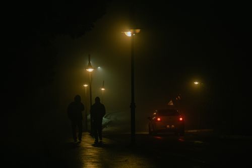 Free Two people walk on a foggy street at night, illuminated by streetlights. Stock Photo