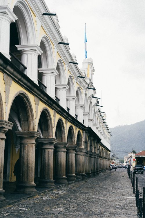 Free Historic colonial building with arches in Antigua, Guatemala, featuring the national flag. Stock Photo
