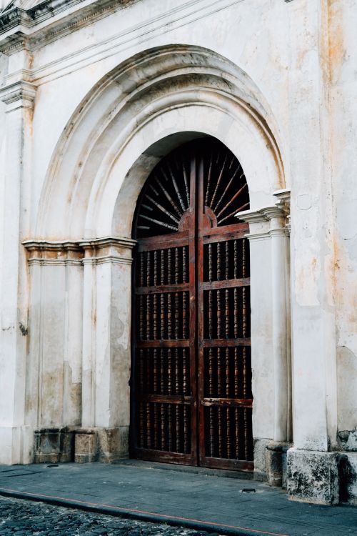 Free A detailed view of a rustic wooden door set in an arched stone frame, typical of Antigua Guatemala's colonial architecture. Stock Photo