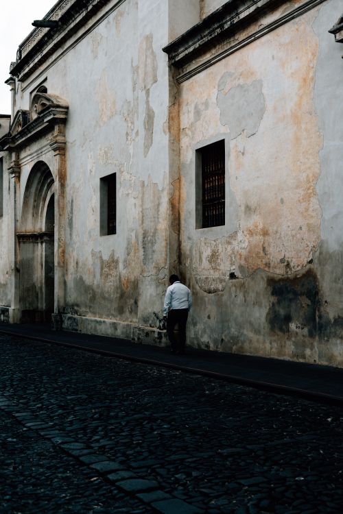 Free A person walks past a weathered historic wall in Antigua Guatemala, showcasing old-world charm. Stock Photo