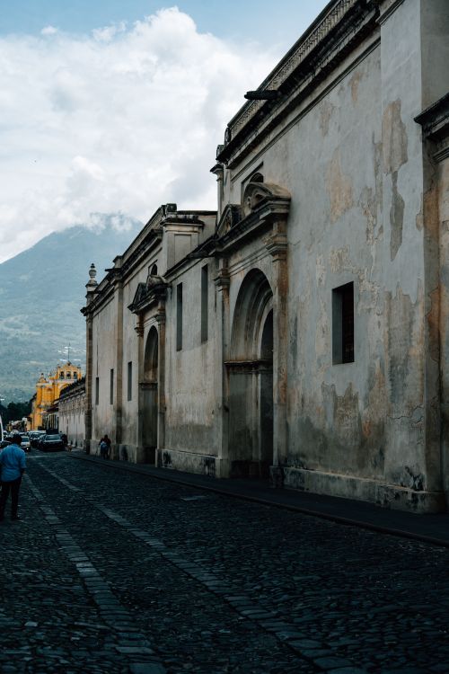 Free Historic street scene in Antigua Guatemala showcasing colonial architecture and distant mountains. Stock Photo