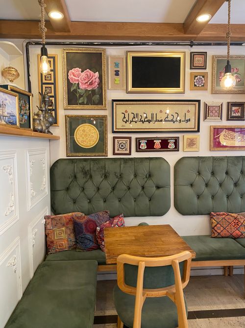 Free Charming café corner with green seating, art frames, and cozy lighting, offering a warm and inviting atmosphere. Stock Photo