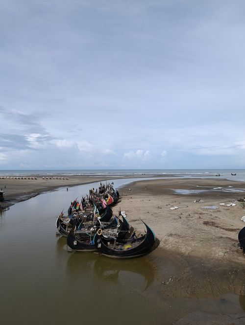 Free Rows of traditional fishing boats rest on a sandy shore under a cloudy sky, creating a serene coastal scene. Stock Photo
